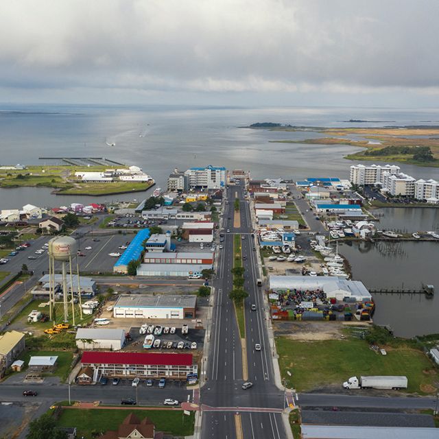 Aerial view of a small coastal community. A four-lane divided road runs through the center of the downtown commercial area surrounded on three sides by the waters and marshes of the Chesapeake Bay.