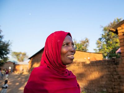 a woman standing in front of a brick wall wearing a red head scarf.