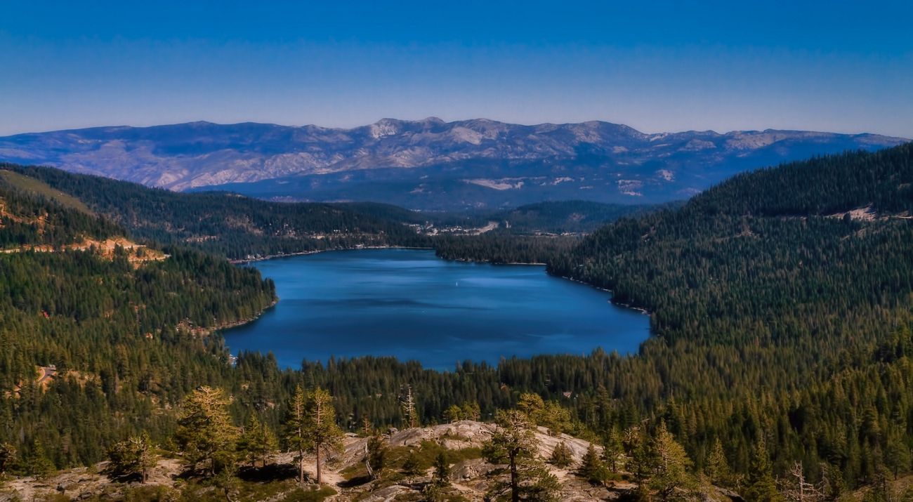 Aerial view looking down on Donner Lake, surrounded by the heavily forested ridges of the northern Sierra Mountains.