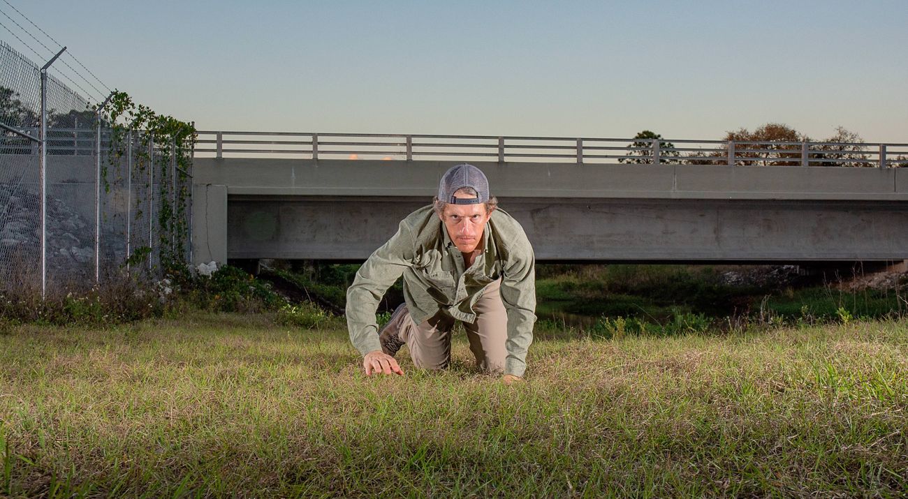Man crawls toward the camera with overpass behind