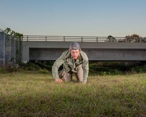 Man crawls toward the camera with overpass behind