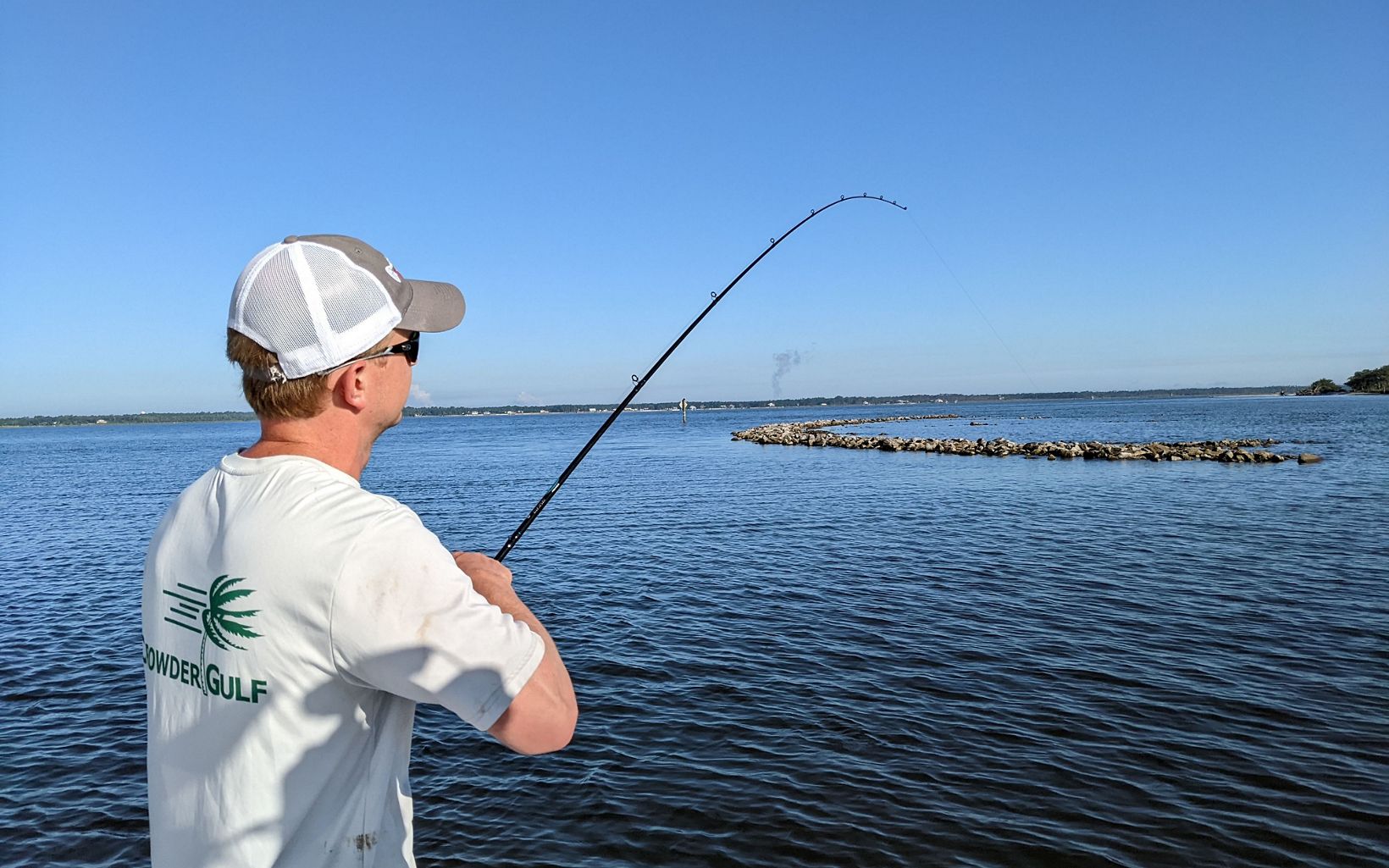 A man fishes from a boat with his rod bent towards the newly constructed oyster reefs. 
