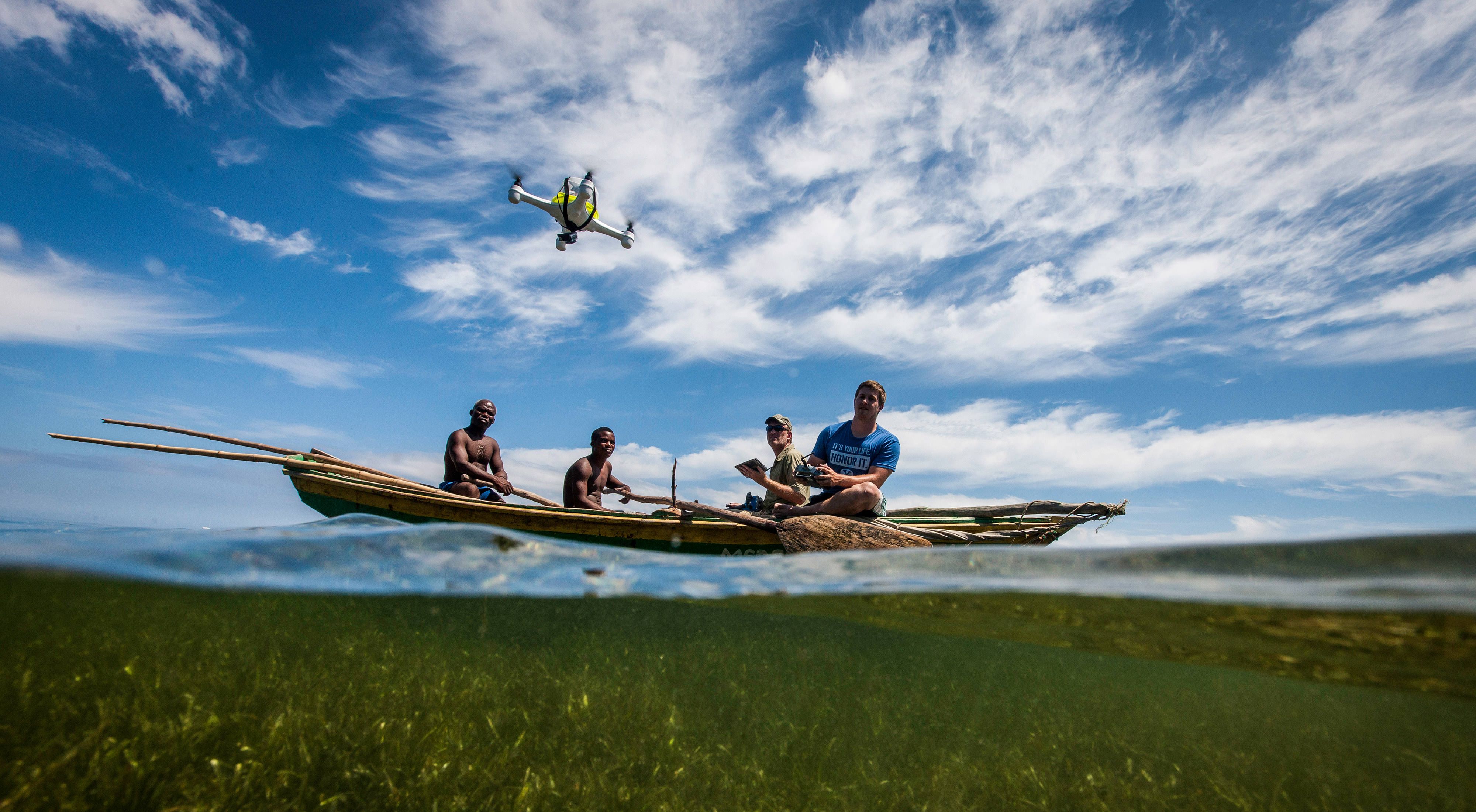 Four people sit in a boat on the water and use an air drone to monitor wetlands in Haiti.