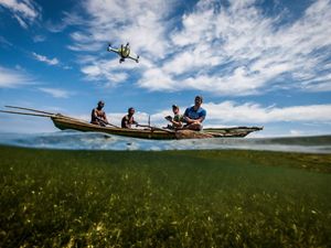 four men sit on a boat and pilot a drone against a blue sky