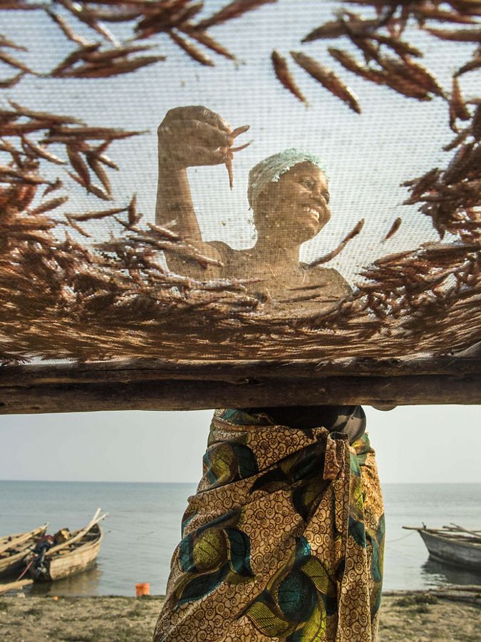 A woman smiles as she lays sardines on drying racks