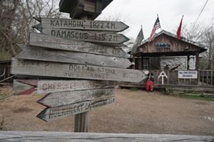A wooden waypost sign in the foreground show distances to points along the Appalachian Trail. A rustic general store is in the background.