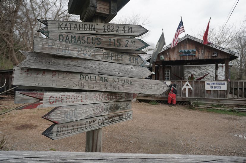 A wooden waypost sign in the foreground show distances to points along the Appalachian Trail. A rustic general store is in the background.