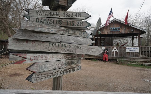 A wooden waypost sign in the foreground show distances to points along the Appalachian Trail. A rustic general store is in the background.