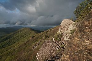 Gray clouds hang heavy and low along a forested mountain ridge line.