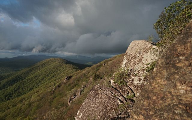 Gray clouds hang heavy and low along a forested mountain ridge line.