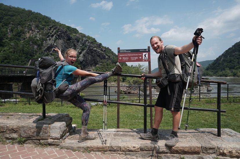 A woman and man celebrate and pose next to a sign marking the midpoint of the Appalachian Trail in Harpers Ferry, WV.