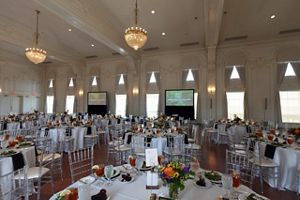 A large ballroom filled with circular tables, screens and a stage. 