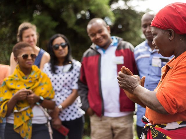 a woman stands in the foreground and instructs a crew of people in a training.
