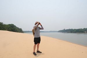 Mauro Salazar observa con binoculares la lejanía en el borde de una duna junto a un río.