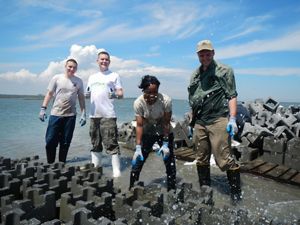 A group of people laugh as they are splashed by small waves while building oyster castles.