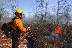 A person in PPE stands in front of a small flame.