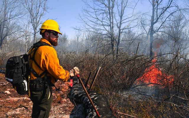 A person in PPE stands in front of a small flame.