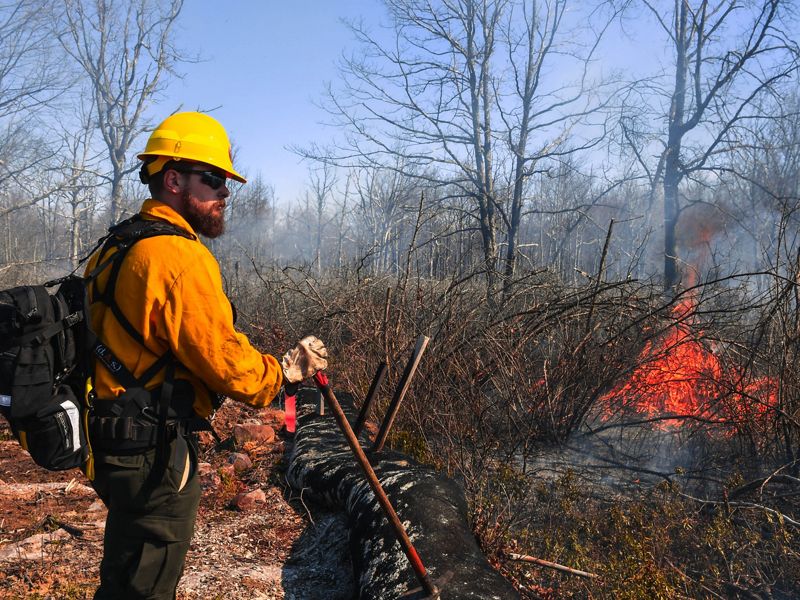 A person in PPE stands in front of a small flame.
