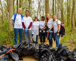 Six people pose together during a stream cleanup event. They are holding large black plastic trash bags and carrying long orange grabbers.