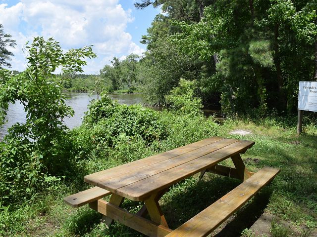 A picnic table sits on grass in front of a body of water.