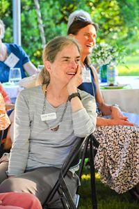 A photo of Beth Hucker sitting in a chair with her head resting in her hand and laughing. 