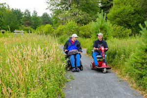 Two people using wheel chairs talk to each other as they explore a nature trail.
