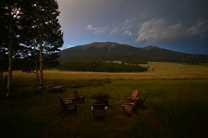 Landscape of a mountain after sunset, with dimly lit lawn chairs in the foreground.