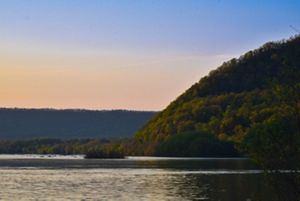 A view of a small mountain sitting in a body of water against a setting sun.