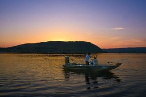 The sunsets over a mountain along the Susquehanna River as a person brings in their boat to a dock.