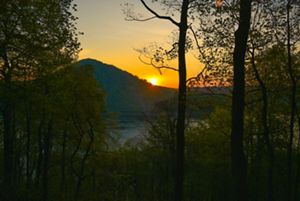 A setting orange sun peeks over a mountain top creating a peacfeul orange glow along the Susquehanna Water Gap.