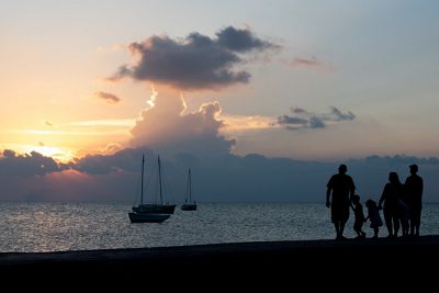 Tres adultos y dos niños se recortan en silueta contra un cielo anaranjado al atardecer mientras caminan por la playa.