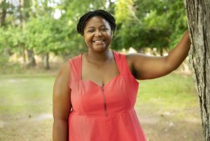 Vanessa Moses headshot. A smiling woman stands next to a tree on the grounds of TNC's Brownsville Preserve.