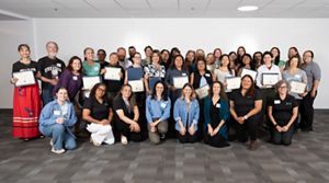 A group of around twenty-five people pose inside for a photo while holding certificates.
