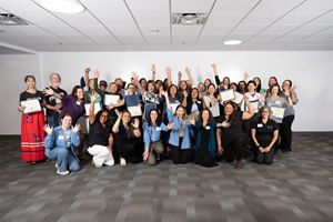 A group of about 40 people pose for a photo with their arms up in celebration.