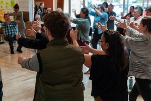 Several people stand in a circle and stretch their arms in front of themselves.