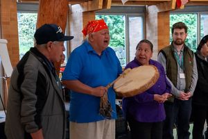 People stand around another person singing and beating a drum.
