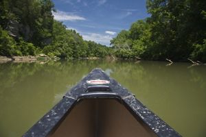 The front of a black kayak points forward on a river.