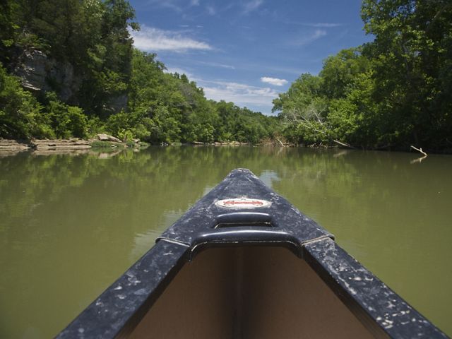 The front of a black kayak points forward on a river.