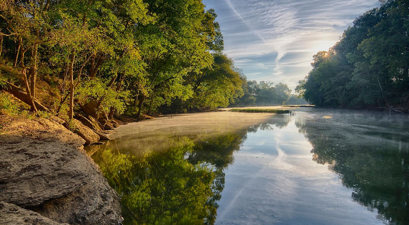 The sun rises over a calm river lined with trees.