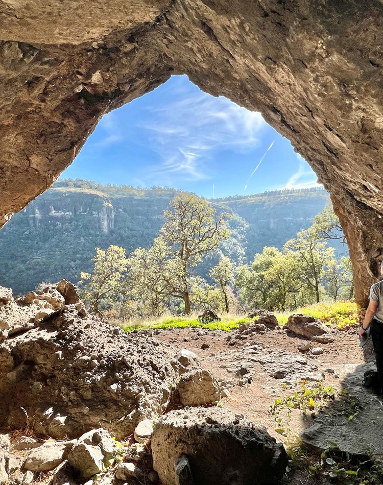 A person stands under a rock overhang on Dye Creek.
