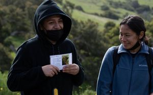 Two students share stories in the field, one of whom holds a card with text and a picture on it.