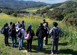 Students gathered outside in a field listening to a guide.