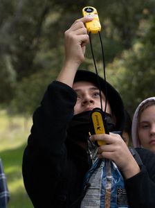 Local student holds and looks up at instrument used to read wind speed.