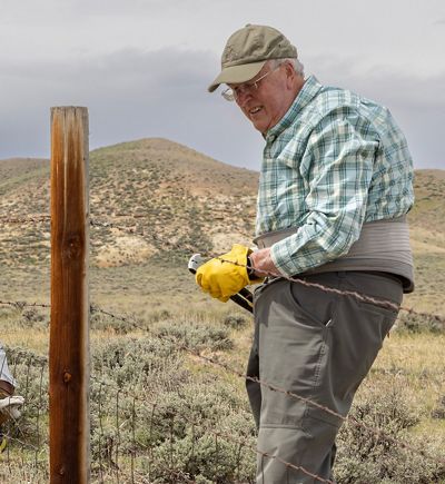 Dave Work mends a wire fence on a prairie.