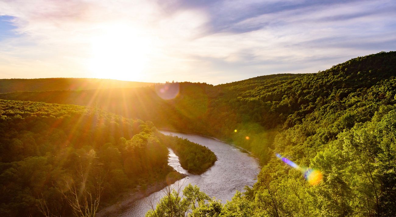 A view of the sun setting over the Delaware River as it meanders between two mountain ranges.