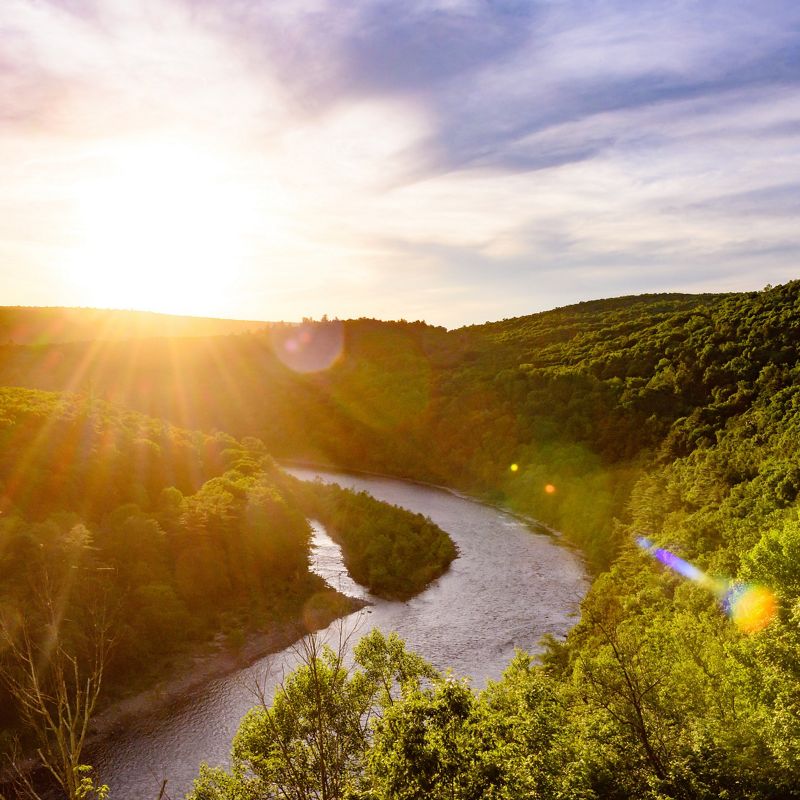 A sun sets over a winding river traveling through the Pocono Mountains.