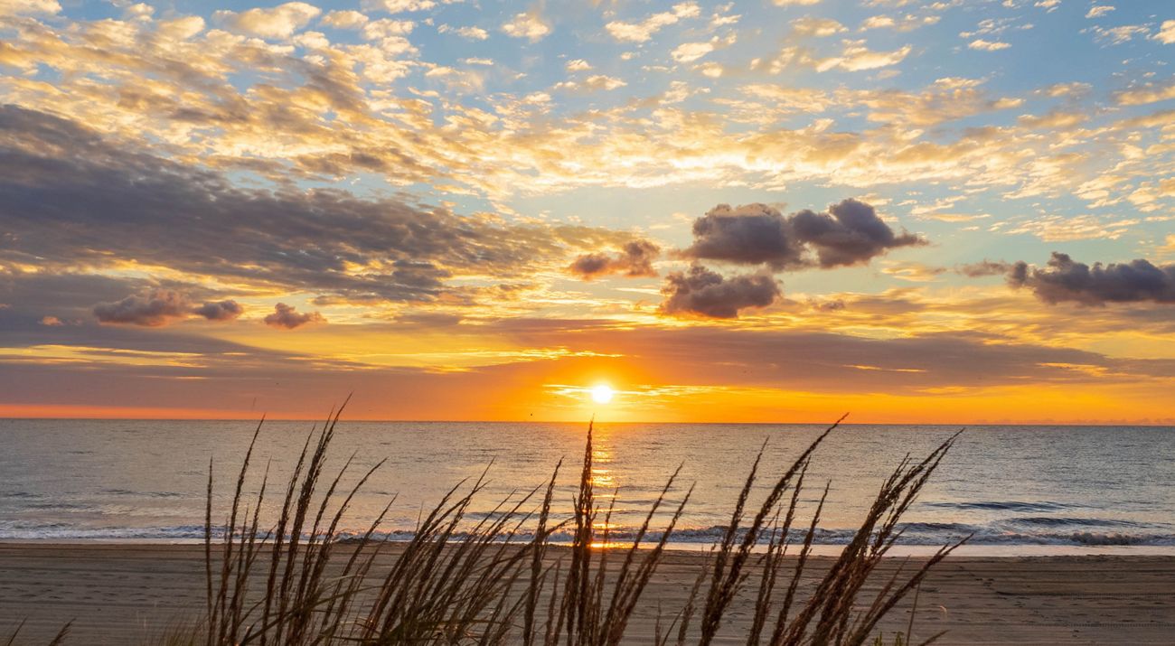 The sun rises over the ocean in Rehoboth Beach creating an orange reflection in the water.