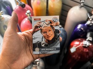 A hand holding out a trading card with an illustration of Jill Heinerth.