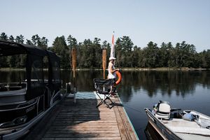 A woman with an orange life preserver standing at the end of a dock.