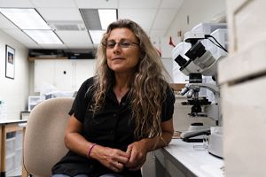 A woman with glasses smiling at the camera in a lab.